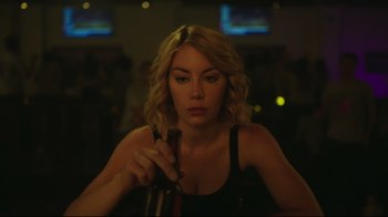 Movie still from “Peacemaker” (2022), created by James Gunn – A woman holding a wine bottle in a room; Close Up shot, Over the shoulder angle