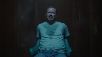 Movie still from “Peacemaker” (2022), created by James Gunn – A man sitting in a chair with his mouth open; Medium shot, Overhead angle