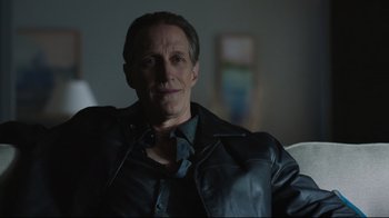 Movie still from “Peacemaker” (2022), created by James Gunn – A man in a leather jacket sitting in a chair; Close Up shot, Over the shoulder angle