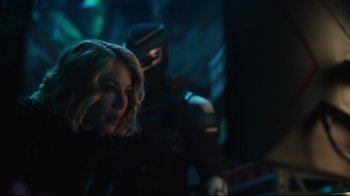 Movie still from “Peacemaker” (2022), created by James Gunn – A woman with blonde hair and a man in a black suit; Close Up shot, Over the shoulder angle
