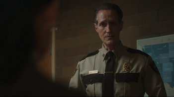 Movie still from “Peacemaker” (2022), created by James Gunn – A man in a sheriff's uniform standing in front of a brick wall; Close Up shot, Over the shoulder angle