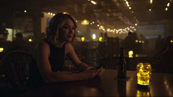 Movie still from “Peacemaker” (2022), created by James Gunn – A woman sitting at a table with a cell phone in her hand; Close Up shot, Over the shoulder angle