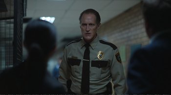 Movie still from “Peacemaker” (2022), created by James Gunn – A man in a uniform standing next to a wall; Medium shot, Over the shoulder angle