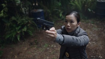 Movie still from “Peacemaker” (2022), created by James Gunn – A woman holding a gun in her hand; Close Up shot, High angle