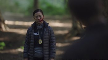 Movie still from “Peacemaker” (2022), created by James Gunn – A woman in a black jacket and a medal in her mouth; Medium shot, Over the shoulder angle