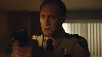 Movie still from “Peacemaker” (2022), created by James Gunn – A man in a police uniform holding a cell phone; Close Up shot, Low angle