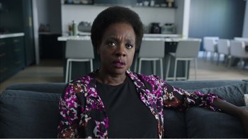 Movie still from “Peacemaker” (2022), created by James Gunn – An older woman sitting on a couch in front of a table; Close Up shot, Over the shoulder angle