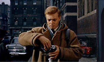 Movie still from “Peeping Tom” (1960), directed by Michael Powell – A man holding a camera while standing on the street; Medium shot, Low angle