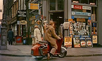 Movie still from “Peeping Tom” (1960), directed by Michael Powell – A man riding a motorcycle down a street; Wide shot, High angle