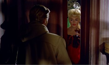 Movie still from “Peeping Tom” (1960), directed by Michael Powell – A man standing in front of a mirror looking at a blonde woman; Medium shot, Over the shoulder angle