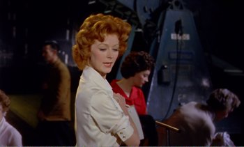 Movie still from “Peeping Tom” (1960), directed by Michael Powell – A woman with red hair and a white shirt is posing; Medium shot, Low angle
