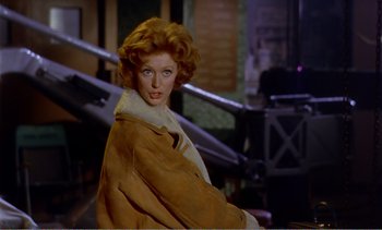 Movie still from “Peeping Tom” (1960), directed by Michael Powell – A woman in a brown coat is posing for a picture; Medium shot, Over the shoulder angle
