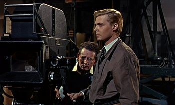 Movie still from “Peeping Tom” (1960), directed by Michael Powell – A man standing next to another man in front of a video camera; Medium shot, Over the shoulder angle