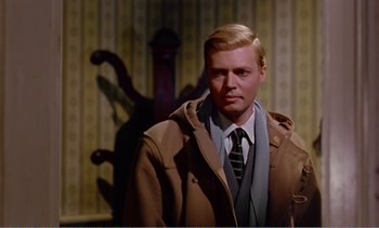 Movie still from “Peeping Tom” (1960), directed by Michael Powell – A man wearing a coat and tie standing in front of a chair; Medium shot, Over the shoulder angle