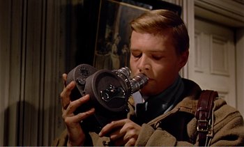 Movie still from “Peeping Tom” (1960), directed by Michael Powell – A man holding an old - fashioned camera in his mouth; Close Up shot, Low angle