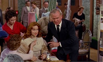 Movie still from “Peeping Tom” (1960), directed by Michael Powell – An older man and a young woman in front of a group of people; Medium shot, Over the shoulder angle