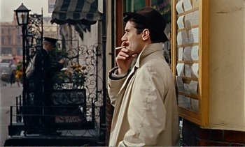 Movie still from “Peeping Tom” (1960), directed by Michael Powell – A man smoking a cigarette while wearing a hat; Medium shot, Over the shoulder angle