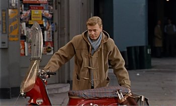 Movie still from “Peeping Tom” (1960), directed by Michael Powell – A man riding a motorcycle down a street; Medium shot, Over the shoulder angle