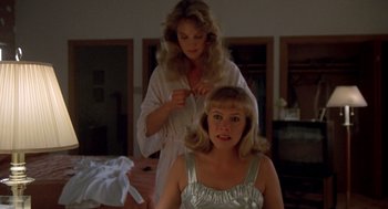 Movie still from “Peggy Sue Got Married” (1986), directed by Francis Ford Coppola – A woman in a white bathrobe is cutting a woman's hair; Medium shot, Over the shoulder angle