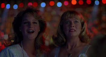 Movie still from “Peggy Sue Got Married” (1986), directed by Francis Ford Coppola – Two women standing next to each other in front of lights; Close Up shot, Low angle