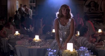 Movie still from “Peggy Sue Got Married” (1986), directed by Francis Ford Coppola – A woman in a silver dress standing in front of a table; Medium shot, Low angle