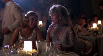Movie still from “Peggy Sue Got Married” (1986), directed by Francis Ford Coppola – Two women sitting at a table in front of candles; Medium shot, Over the shoulder angle