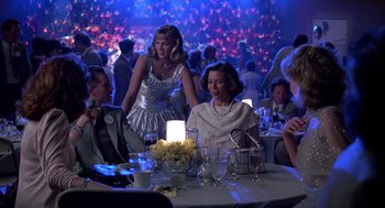 Movie still from “Peggy Sue Got Married” (1986), directed by Francis Ford Coppola – A group of people sitting around a table at a party; Wide shot, Over the shoulder angle