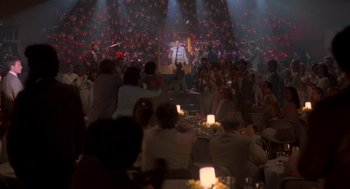 Movie still from “Peggy Sue Got Married” (1986), directed by Francis Ford Coppola – A crowd of people sitting at tables in front of a microphone; Extreme Wide shot, Over the shoulder angle