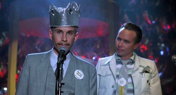 Movie still from “Peggy Sue Got Married” (1986), directed by Francis Ford Coppola – A man wearing a crown and a microphone in front of another man in a suit; Close Up shot, Low angle