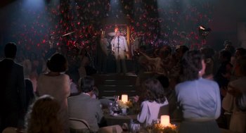 Movie still from “Peggy Sue Got Married” (1986), directed by Francis Ford Coppola – A group of people sitting around a table; Wide shot, Over the shoulder angle
