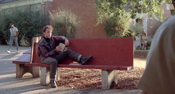 Movie still from “Peggy Sue Got Married” (1986), directed by Francis Ford Coppola – A man sitting on top of a wooden park bench; Wide shot, Low angle