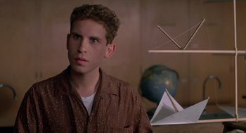 Movie still from “Peggy Sue Got Married” (1986), directed by Francis Ford Coppola – A man in a brown shirt is standing in front of a globe; Close Up shot, Low angle