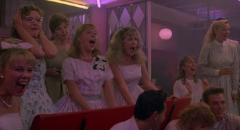 Movie still from “Peggy Sue Got Married” (1986), directed by Francis Ford Coppola – A group of women singing together in a theater; Medium shot, High angle
