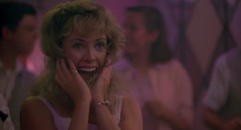 Movie still from “Peggy Sue Got Married” (1986), directed by Francis Ford Coppola – A woman with blonde curly hair smiling at the camera; Close Up shot, Over the shoulder angle
