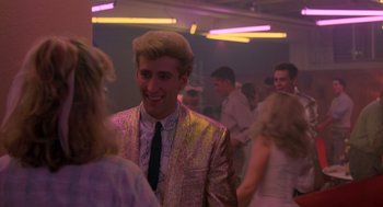 Movie still from “Peggy Sue Got Married” (1986), directed by Francis Ford Coppola – A man in a suit and tie standing next to a woman; Medium shot, Over the shoulder angle