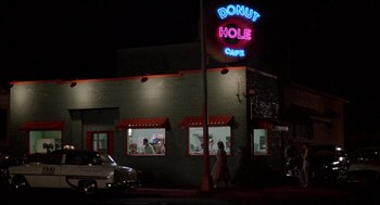 Movie still from “Peggy Sue Got Married” (1986), directed by Francis Ford Coppola – A woman walking in front of a donut hole cafe at night; Extreme Wide shot, Low angle