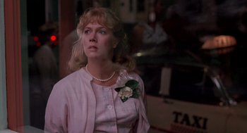 Movie still from “Peggy Sue Got Married” (1986), directed by Francis Ford Coppola – A woman in a pink shirt and a white flower in her hair; Close Up shot, Over the shoulder angle
