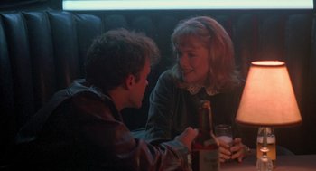 Movie still from “Peggy Sue Got Married” (1986), directed by Francis Ford Coppola – A man and a woman sitting at a table with a bottle of wine; Medium shot, Over the shoulder angle