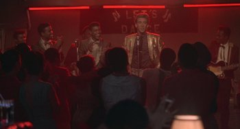 Movie still from “Peggy Sue Got Married” (1986), directed by Francis Ford Coppola – A couple of men singing into microphones in front of an audience; Medium shot, Over the shoulder angle
