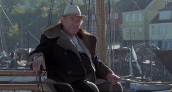 Movie still from “Pelle the Conqueror” (1987), directed by Bille August – An older man sitting on top of a boat in the water; Medium shot, High angle