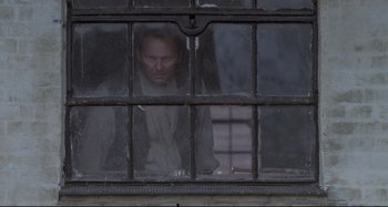 Movie still from “Pelle the Conqueror” (1987), directed by Bille August – A man looking out of a window in a building; Medium shot, Low angle