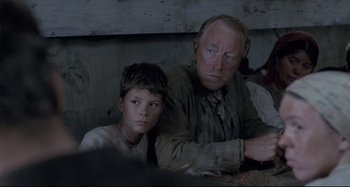 Movie still from “Pelle the Conqueror” (1987), directed by Bille August – A man sitting next to a young boy in front of a wall; Close Up shot, Over the shoulder angle