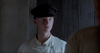 Movie still from “Pelle the Conqueror” (1987), directed by Bille August – A man wearing a black hat standing in front of a wooden wall; Close Up shot, Low angle