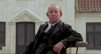 Movie still from “Pelle the Conqueror” (1987), directed by Bille August – An older man sitting in a chair wearing a suit and tie; Close Up shot, Low angle