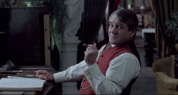Movie still from “Pelle the Conqueror” (1987), directed by Bille August – An older man sitting at a piano in a room; Medium shot, Over the shoulder angle