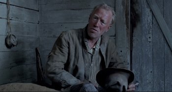 Movie still from “Pelle the Conqueror” (1987), directed by Bille August – An older man sitting in front of a wooden wall holding a hat; Close Up shot, Low angle