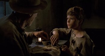 Movie still from “Pelle the Conqueror” (1987), directed by Bille August – A young boy sitting at a table with an older man; Medium shot, Over the shoulder angle