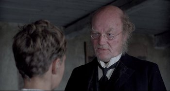 Movie still from “Pelle the Conqueror” (1987), directed by Bille August – An older man wearing a suit and a tie talking to a younger man; Close Up shot, Over the shoulder angle