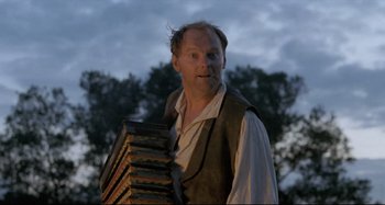 Movie still from “Pelle the Conqueror” (1987), directed by Bille August – A man holding a stack of books in his hands; Medium shot, Low angle