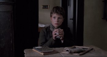 Movie still from “Pelle the Conqueror” (1987), directed by Bille August – A boy sitting at a table drinking a cup of coffee; Medium shot, High angle